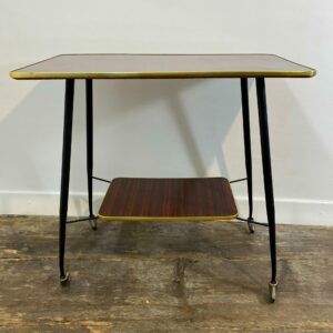 Vintage mid-century modern side table from 1950s with wood veneer top, brass trim edging, black metal legs and rolling casters - retro furniture collectible